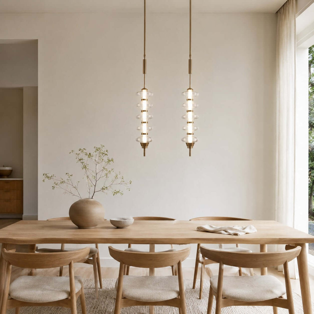 Two gold and clear Clérachic pendants, tall and slim with stacked glass discs, hung above a pale oak dining table.