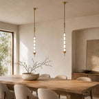A pair of gold and clear Clérachic pendants of stacked glass discs, hanging in a plastered dining room with a window and arched niche.