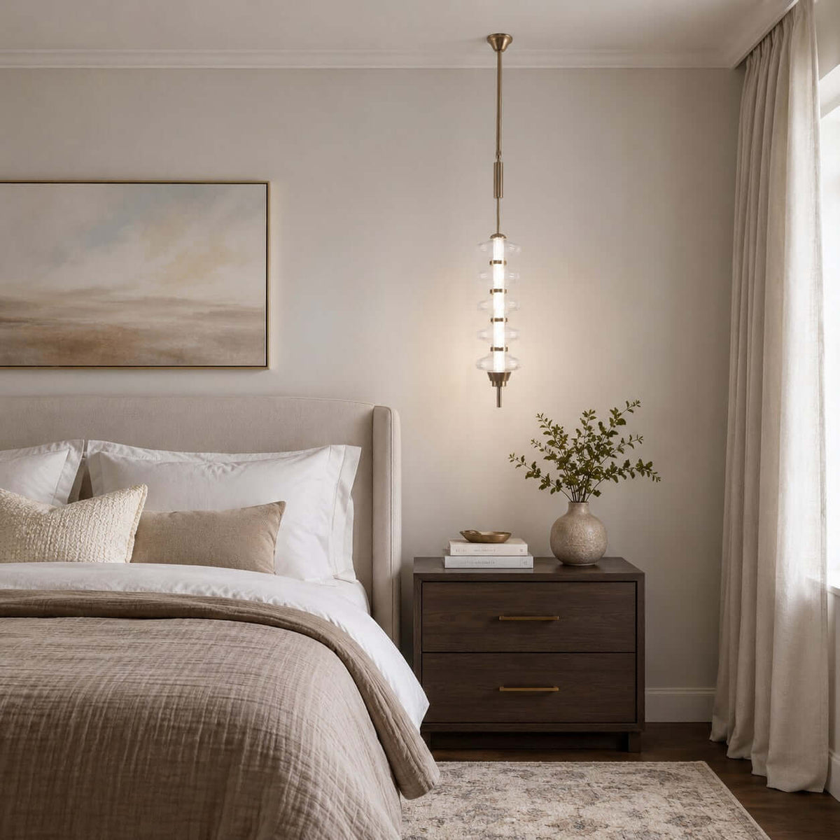 A gold and clear Clérachic pendant lit beside a bed, hung at the height of the nightstand with a vase of stems below.