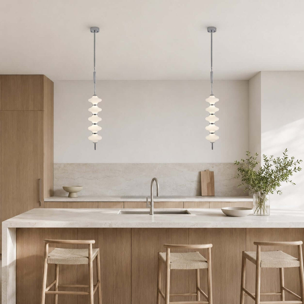 Two chrome and white Clérachic pendants hung over a stone kitchen island, with woven-seat wooden stools and a sink behind.