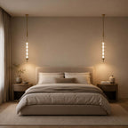 Two gold and clear Clérachic pendants either side of a bed in a dim, warm bedroom, lit like bedside lamps.