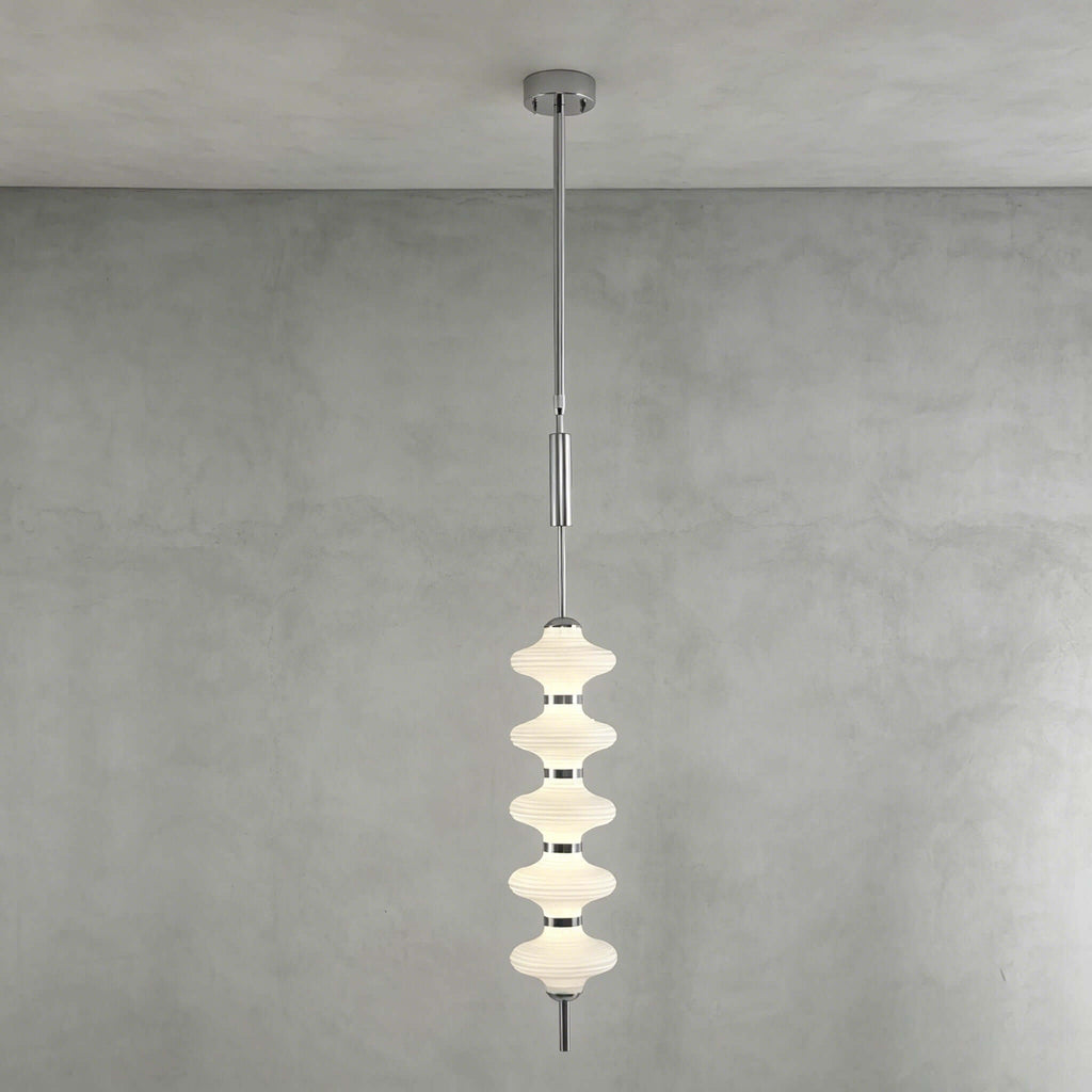 Chrome and white Clérachic pendant of stacked ribbed frosted discs, lit and hanging from its canopy against a grey plaster wall.