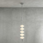 Chrome and white Clérachic pendant of stacked ribbed frosted discs, lit and hanging from its canopy against a grey plaster wall.