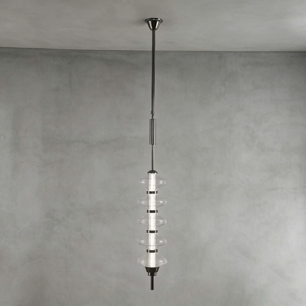 Black and clear Clérachic pendant with stacked clear glass discs around a dark core, hung against a grey plaster wall.