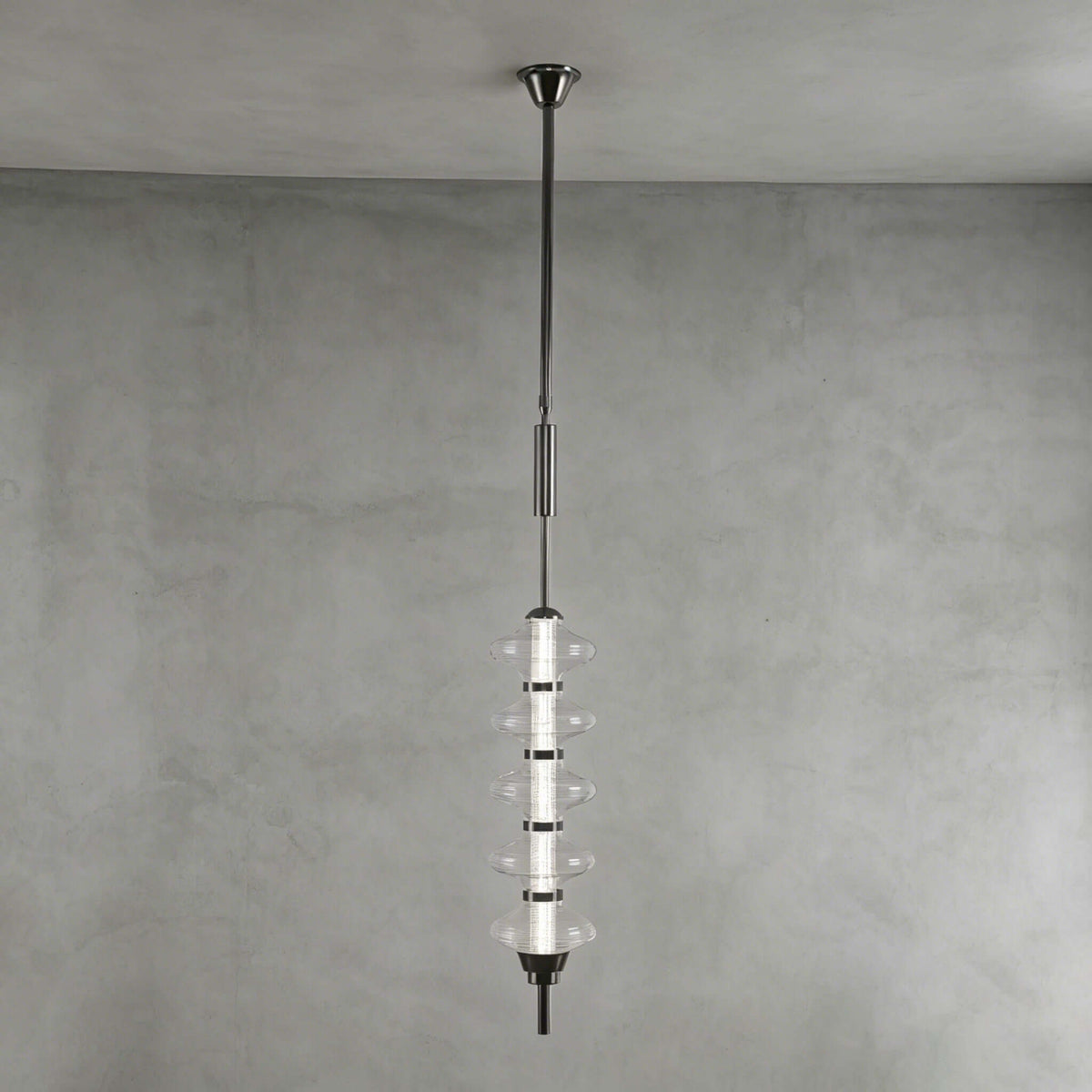 Black and clear Clérachic pendant with stacked clear glass discs around a dark core, hung against a grey plaster wall.