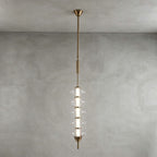 Gold and clear Clérachic pendant with stacked clear discs around a lit centre, on a long gold rod against a grey plaster wall.