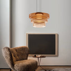Amber Clérachic Stacked Glass Disc Pendant Light glowing beside a shearling armchair and a dark canvas in a quiet living room.