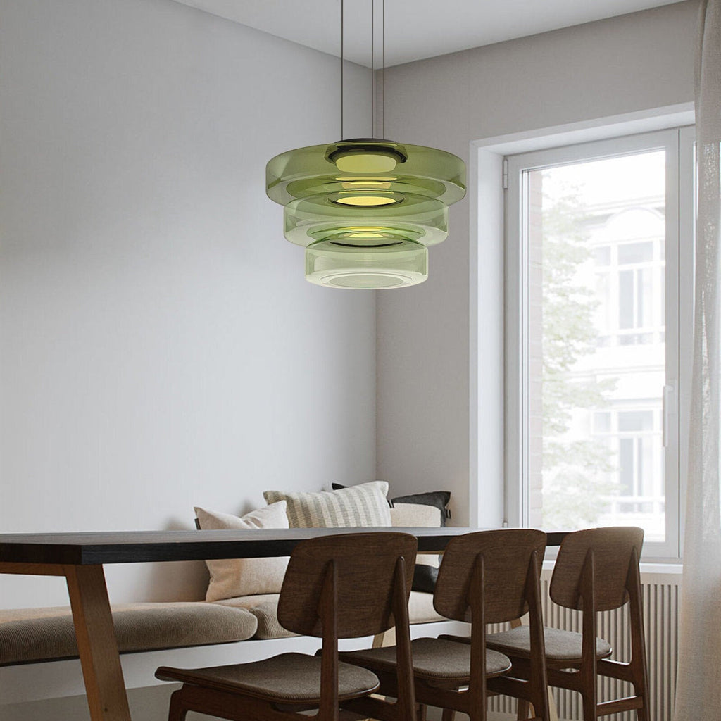 Green Clérachic Stacked Glass Disc Pendant Light hanging over a dark dining table beside a bright full-height window.