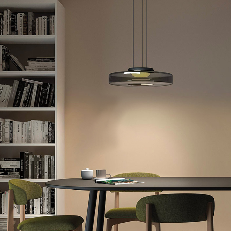 Clérachic Stacked Glass Disc Pendant Light in Smoke Gray over a round dining table, green chairs and a bookcase behind it.