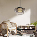 Two-tier Smoke Gray Clérachic Stacked Glass Disc Pendant Light lighting a reading corner with a rattan chair and stacked books.