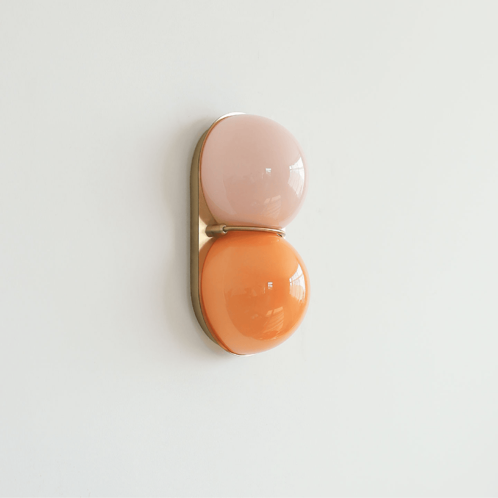 This Clérachic sconce in blush pink over apricot orange glass, on a gold-toned backplate against a pale grey-white wall.