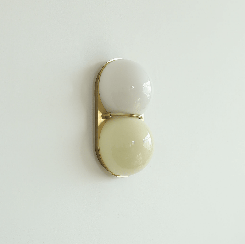 Pale grey-white globe over a soft butter-yellow globe on a gold-toned plate, this Clérachic wall light hangs on a mint-tinted wall.