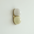 Pale grey-white globe over a soft butter-yellow globe on a gold-toned plate, this Clérachic wall light hangs on a mint-tinted wall.