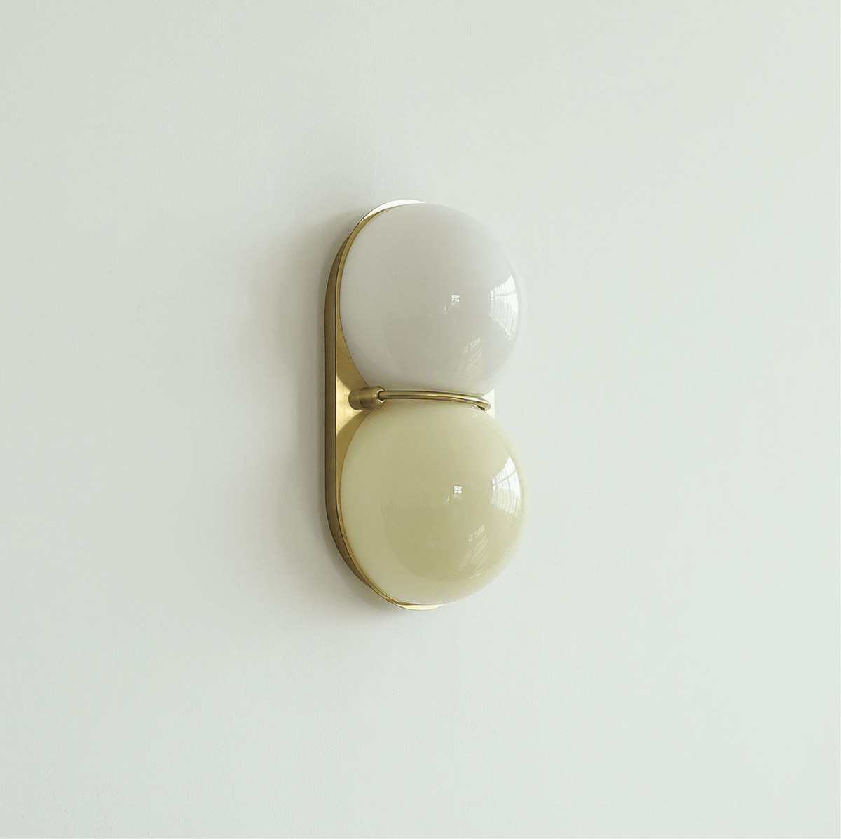 Pale grey-white globe over a soft butter-yellow globe on a gold-toned plate, this Clérachic wall light hangs on a mint-tinted wall.