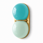 Close angle on a turquoise and mint Clérachic sconce, its gold-toned plate and slim bar catching the light on a white ground.