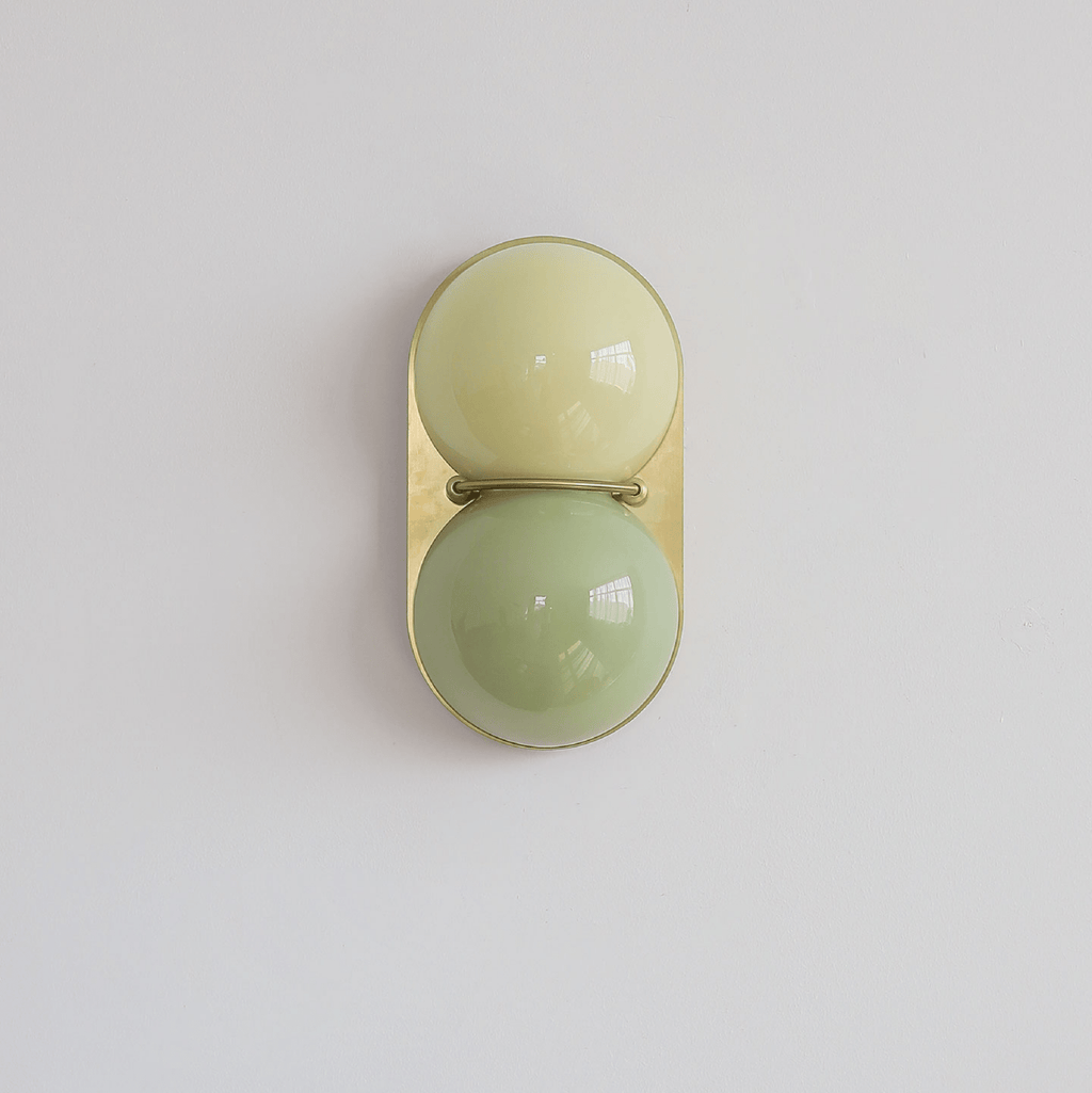 A sage-green lower globe under a pale yellow-green upper globe on a gold-toned plate, this Clérachic sconce seen straight on.