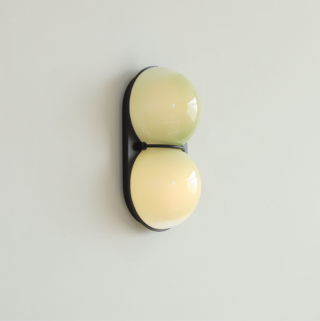 Side-on view of a Clérachic sconce in two soft yellow-green tones, set on a black backplate against a pale mint wall.