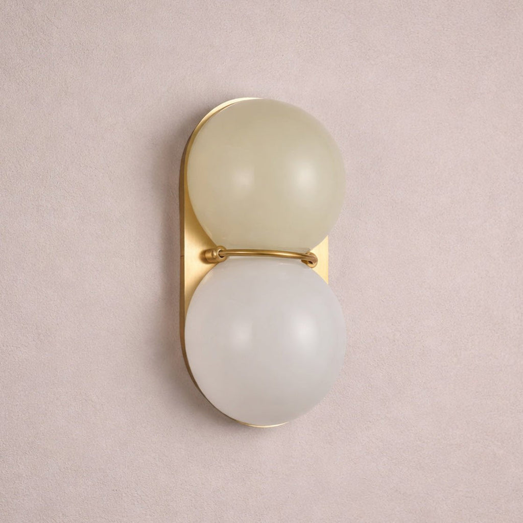 Muted greige globe over a white one on a gold-toned plate, this Clérachic sconce is seen against a dusty pink wall.