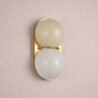 Muted greige globe over a white one on a gold-toned plate, this Clérachic sconce is seen against a dusty pink wall.