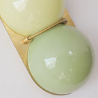 Close view of the brass-coloured bar clasping two yellow-green glass globes on this Clérachic wall light's gold-toned plate.