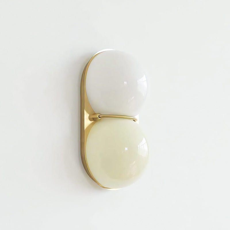 Slightly angled Clérachic sconce with a white upper globe and a pale cream lower globe on a gold-toned plate.