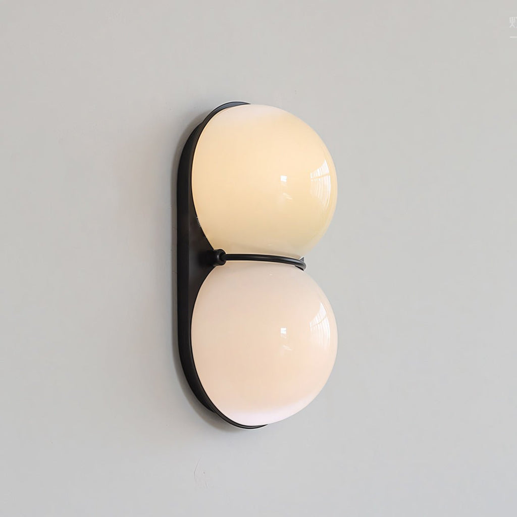 Switched on, this Clérachic wall light shows warm cream light through two glass globes on a black oval backplate.