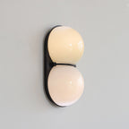 Switched on, this Clérachic wall light shows warm cream light through two glass globes on a black oval backplate.