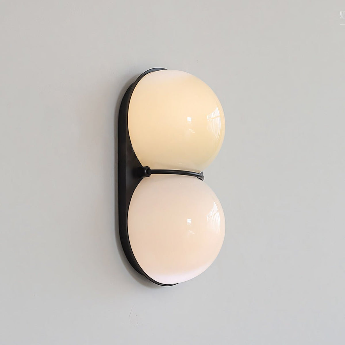 Switched on, this Clérachic wall light shows warm cream light through two glass globes on a black oval backplate.