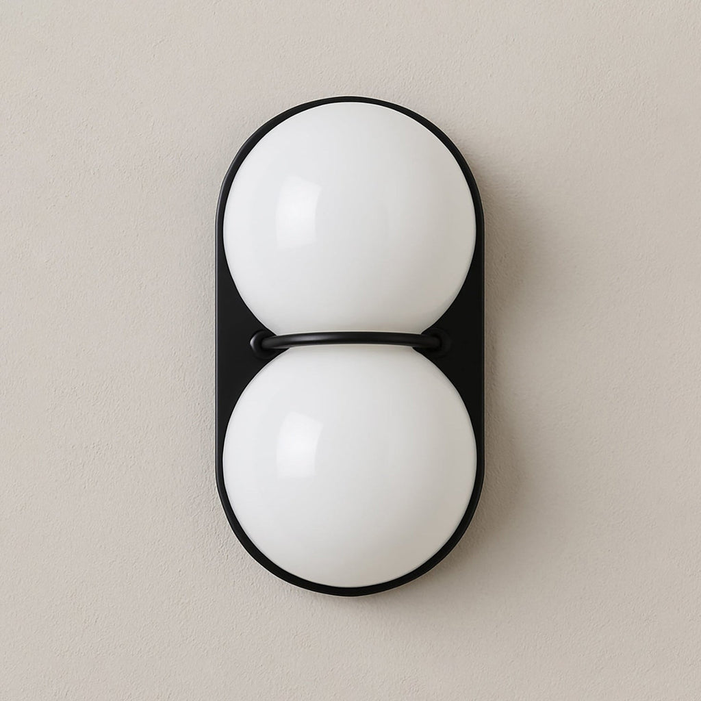 Opaque white globes stacked on a black oval plate, this Clérachic wall light is shown close up on a warm taupe wall.