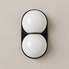 Opaque white globes stacked on a black oval plate, this Clérachic wall light is shown close up on a warm taupe wall.
