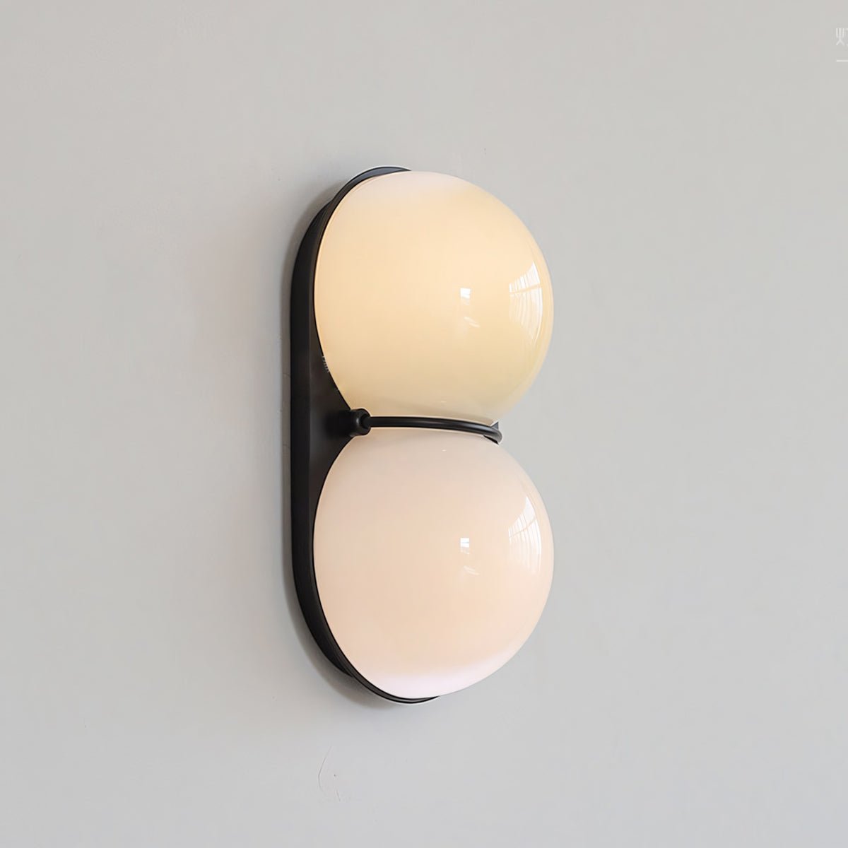 Glowing cream and blush-peach globes light up this Clérachic wall light, angled slightly on a pale grey wall.