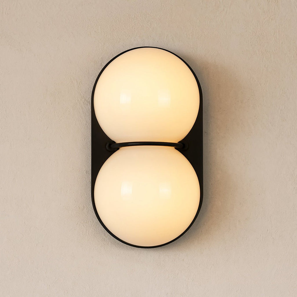 Warm cream light fills both globes of this Clérachic wall light, mounted on a black plate against a beige wall.