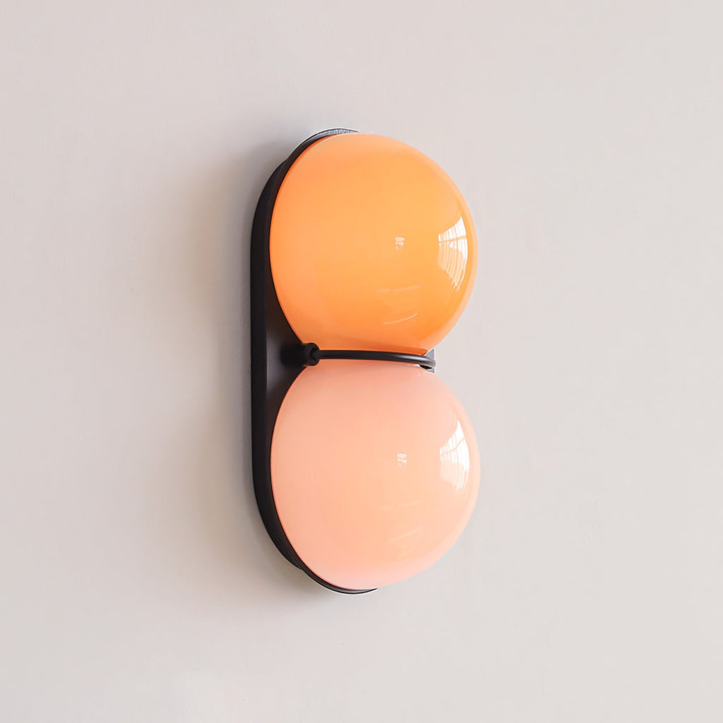 Orange over peach-pink glass on a black oval plate, this Clérachic wall light is photographed on a pale lilac-grey wall.