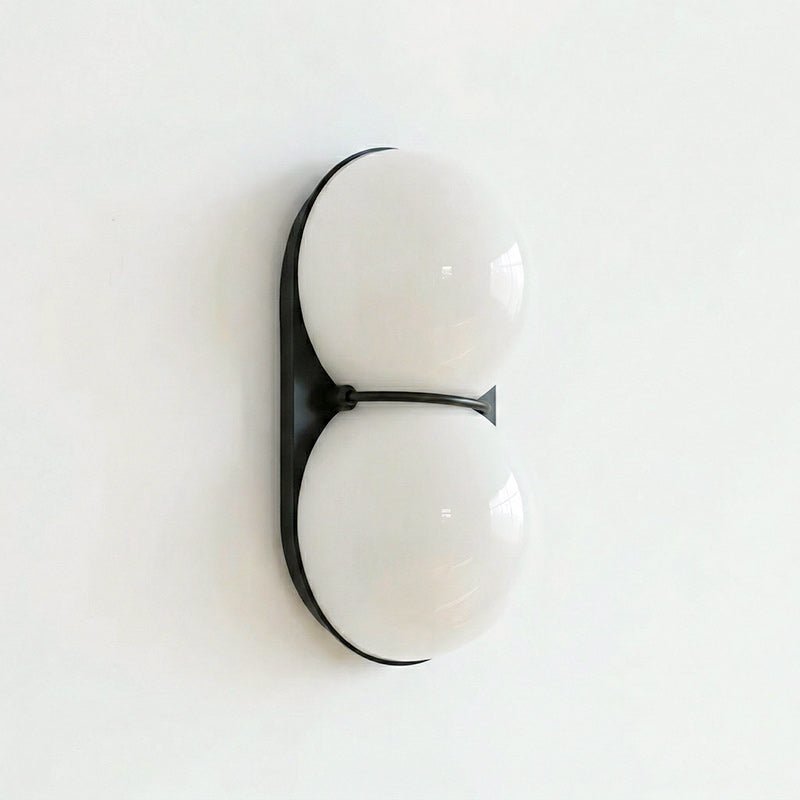 Slightly angled Clérachic wall light with frosted white-grey globes on a black oval plate, against a clean white wall.