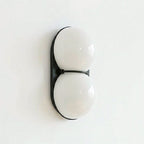 Slightly angled Clérachic wall light with frosted white-grey globes on a black oval plate, against a clean white wall.