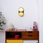 High on a white wall above a walnut sideboard, this Clérachic sconce has pale yellow glass globes on a black plate.