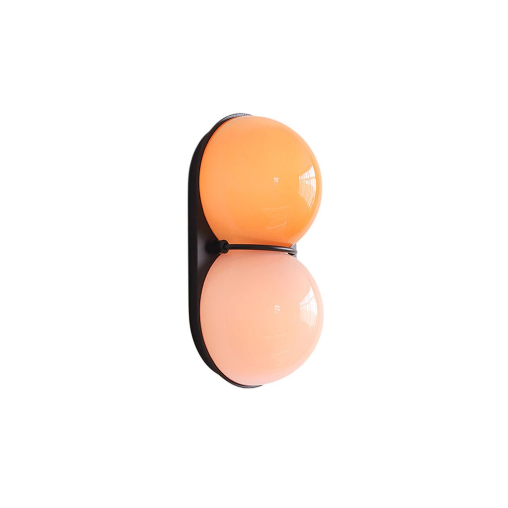 Orange and pink-peach glass globes on a black oval plate, this Clérachic wall light shown cut out on a plain white ground.