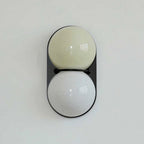 Pale olive globe over a white globe on a black oval backplate, this Clérachic wall light is shown against a pale mint wall.