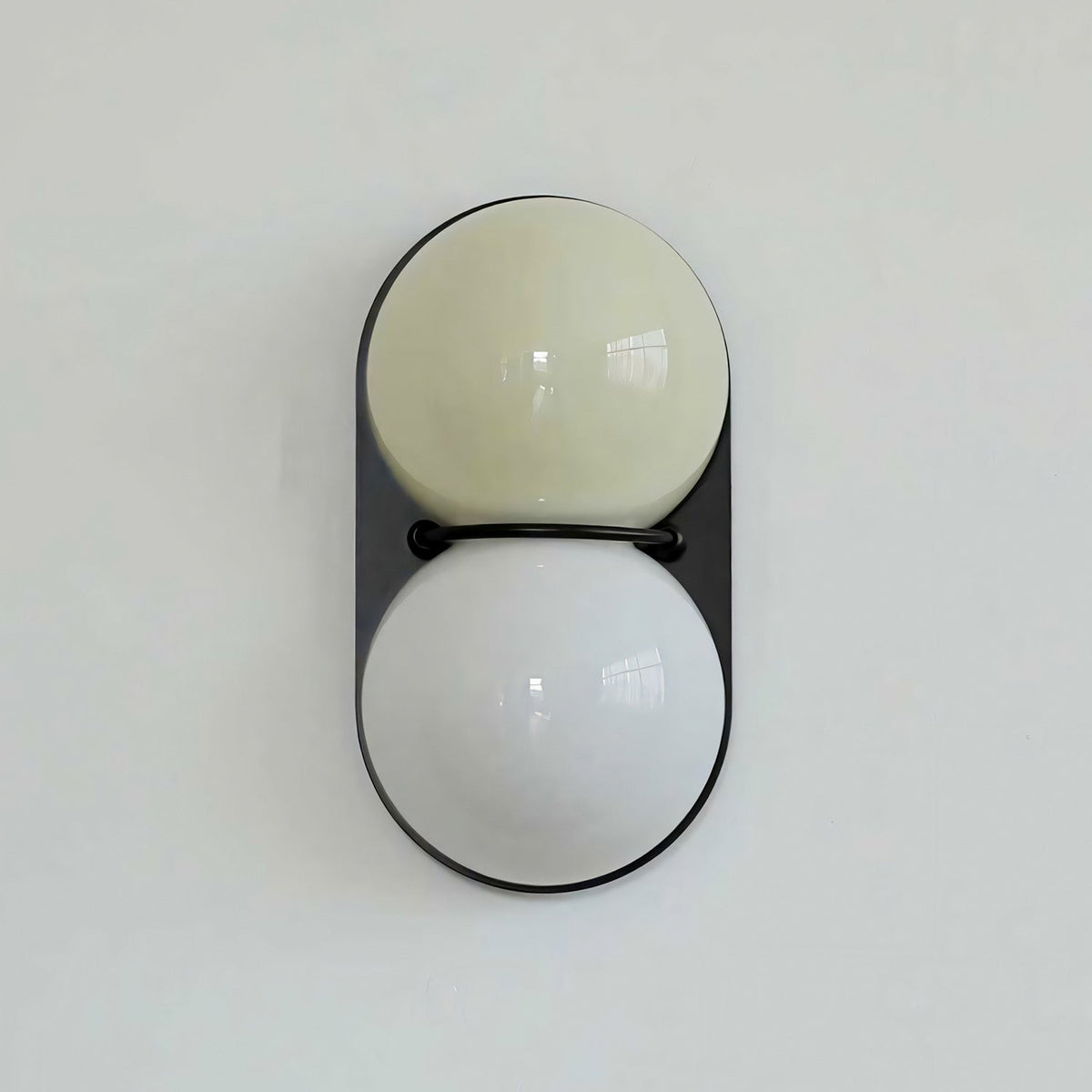 Pale olive globe over a white globe on a black oval backplate, this Clérachic wall light is shown against a pale mint wall.