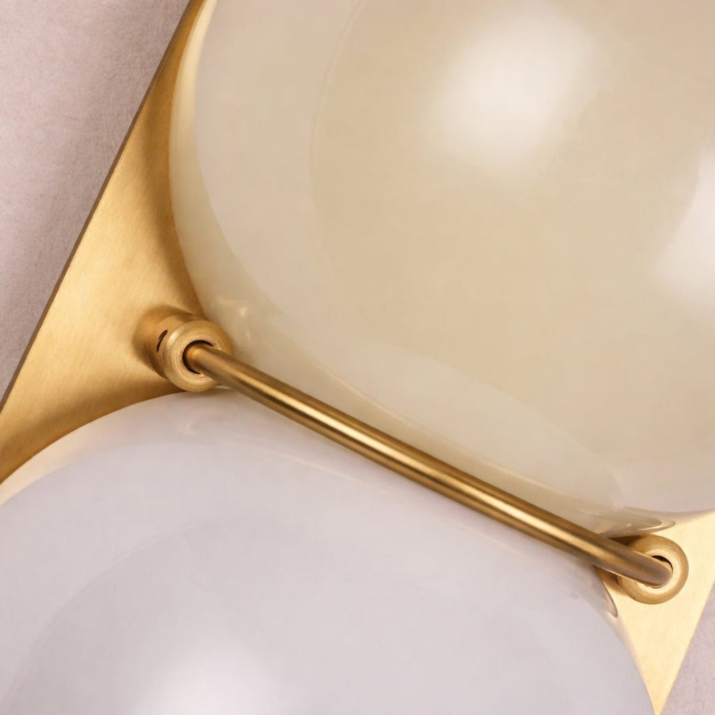 Close view of the brass-coloured bar and gold-toned plate holding cream and white globes on this Clérachic wall light.
