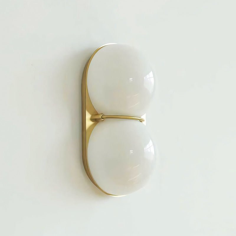 Gold-toned oval plate with two white frosted globes, this Clérachic sconce hangs against a pale mint-white wall.