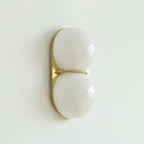 Gold-toned oval plate with two white frosted globes, this Clérachic sconce hangs against a pale mint-white wall.