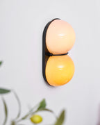 With a faint lemon plant in the foreground, this Clérachic sconce glows peach above and amber below on a black oval plate.