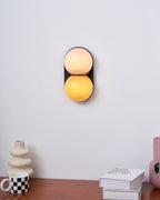 Lit Clérachic wall light with a peach upper globe and amber lower globe above a walnut desk with a checked mug and books.