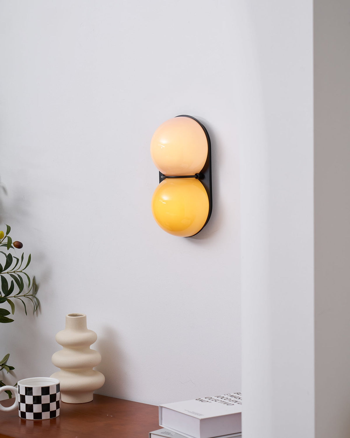 Seen from the left, a glowing peach and amber Clérachic sconce hangs above a desk with a cream vase and checked mug.
