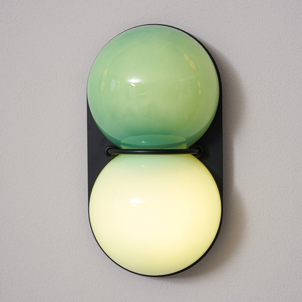 Close up, the lit lower globe of this Clérachic sconce glows creamy yellow-green beneath a green-tinted upper globe.