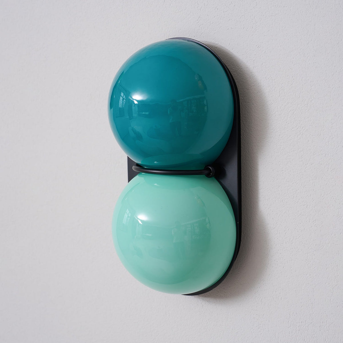 Deep teal upper globe and a light aqua lower globe on a black plate, this Clérachic wall light viewed from the side.