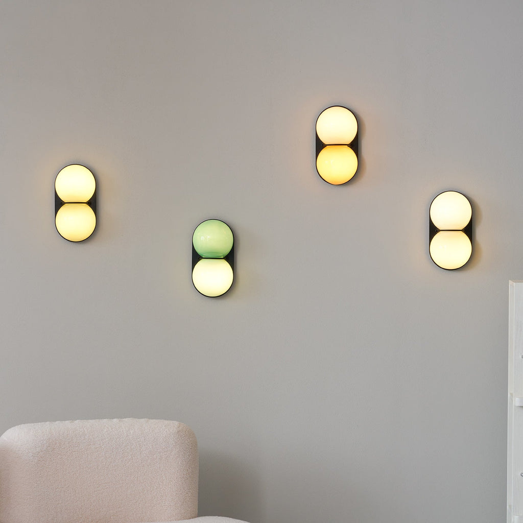 Four Clérachic sconces glowing at different heights on a grey wall above a cream bouclé armchair.