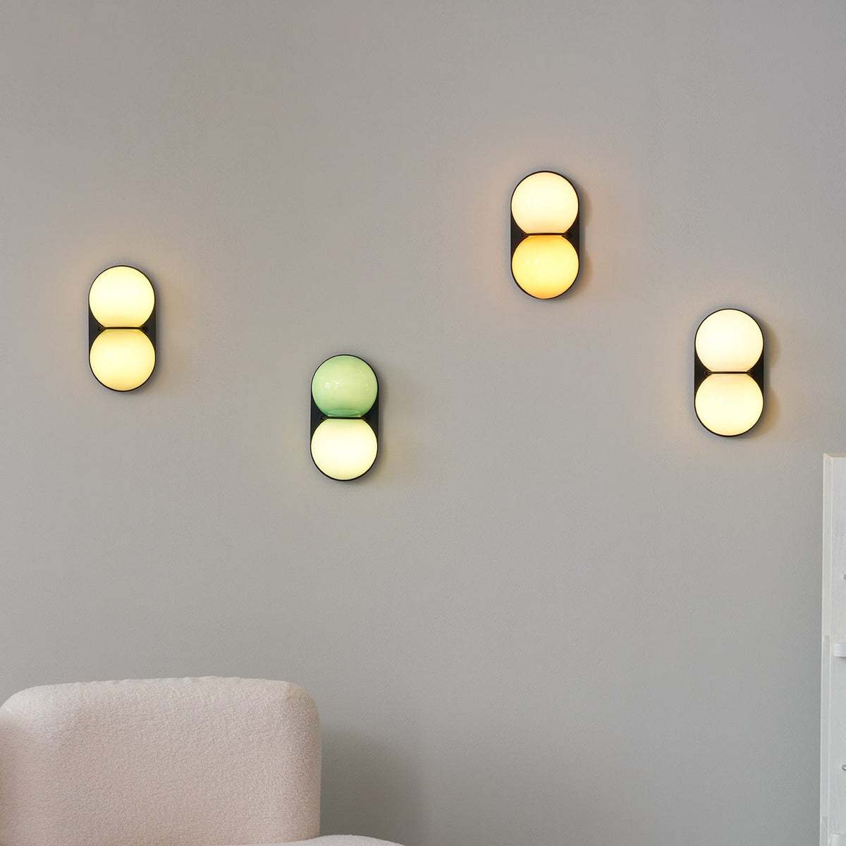 Four Clérachic sconces glowing at different heights on a grey wall above a cream bouclé armchair.