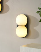 One lit cream Clérachic wall light close up on a pale wall, with another sconce edging into the corner of the frame.